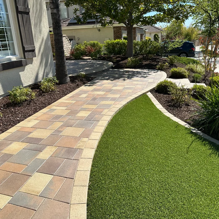 Curved paver walkway with artificial turf front yard landscape design