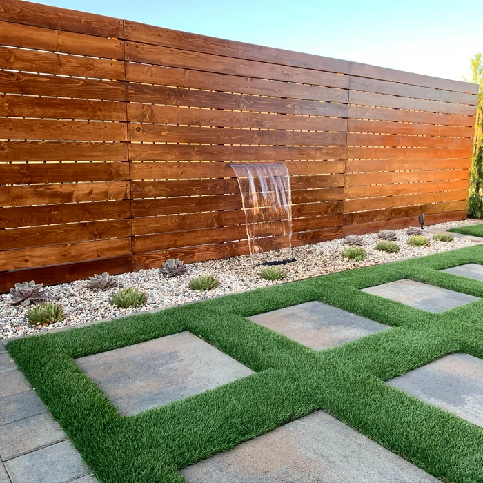 Terraced backyard with wood feature wall, waterfall, artificial turf and pavers